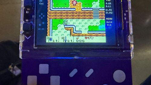 Конференционный бейдж с цветным экраном, на котором идёт Zelda, и сенсорными кнопками под дисплеем.